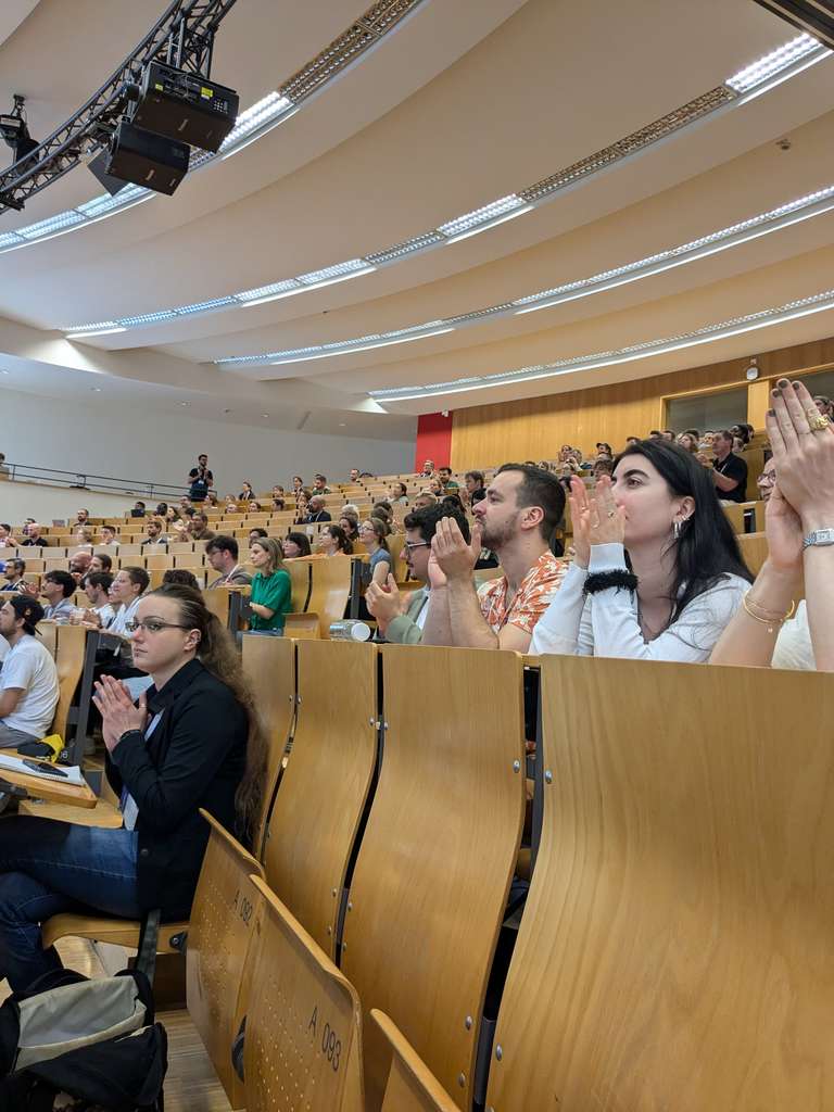 Viele Menschen sitzen in einem Saal in Reihen und schauen gebannt nach vorn.