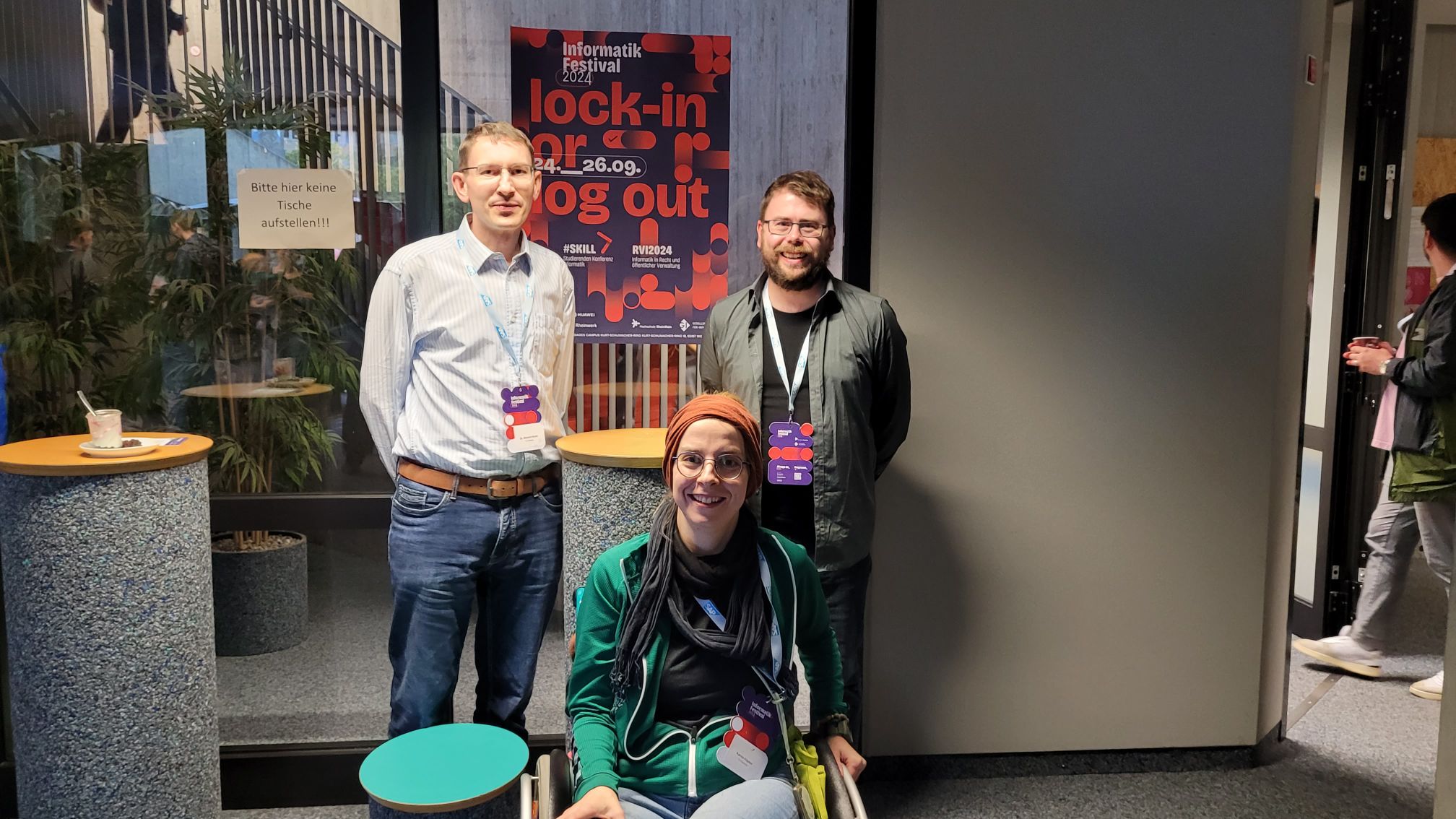 Albrecht, Karola und Andy auf dem Informatik Festival 2024, im Hintergrund das Plakat des Festivals: "lock-in or log out"