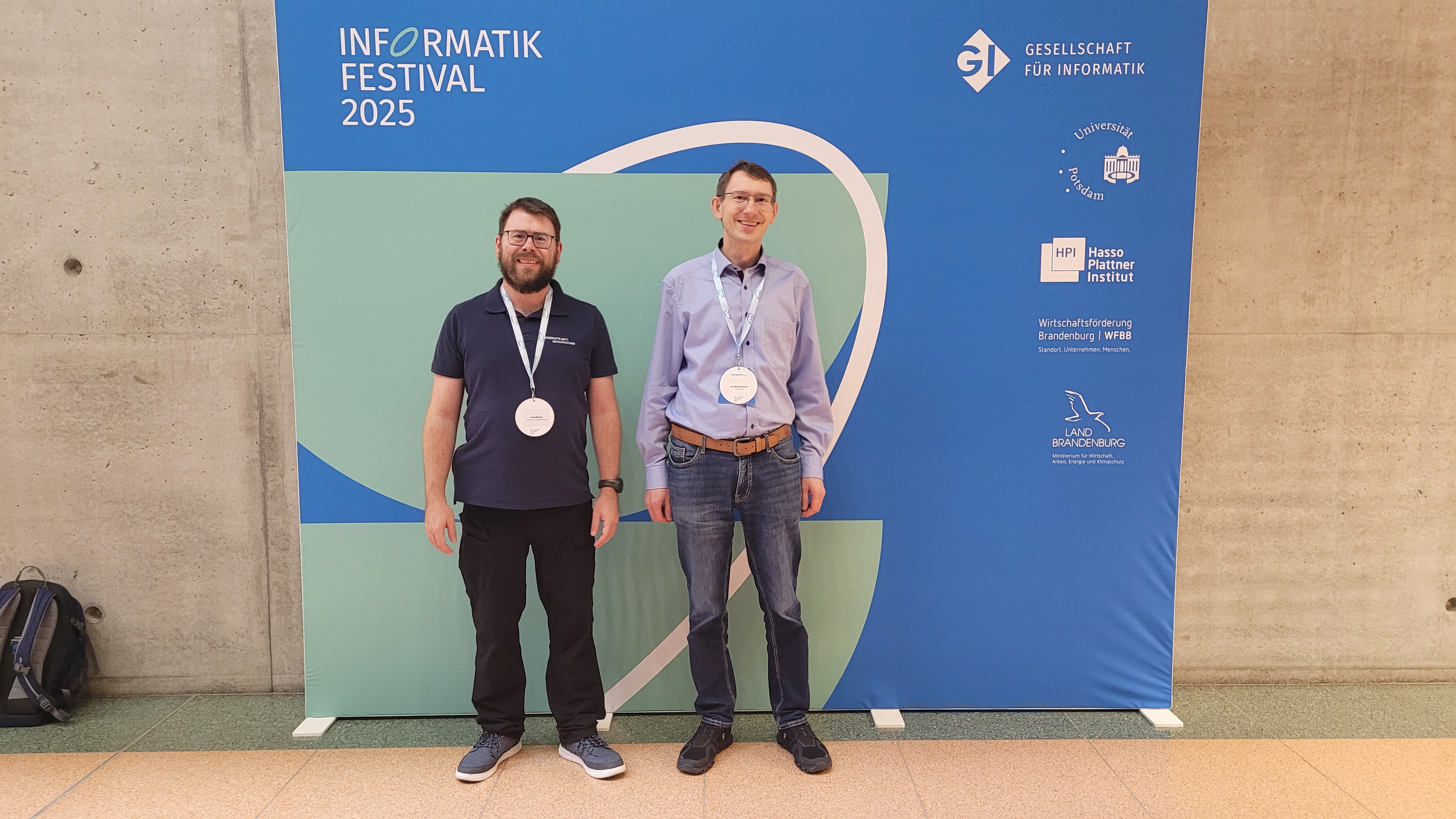 Andy und Albrecht vor einem Banner mit dem Logo des Informatik Festivals 2025