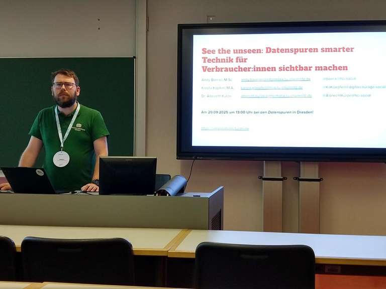 Andy neben einer angebeamten Vortragsfolie mit dem Titel: See the unseen: Datenspuren einfacher Technik für Verbraucher:innen sichtbar machen