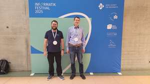 Andy und Albrecht vor einem Banner mit dem Logo des Informatik Festivals 2025